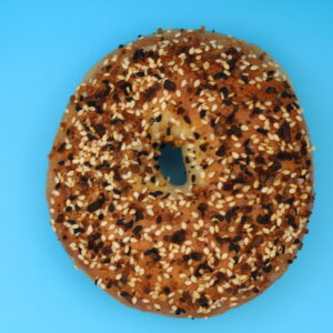 Everything bagel topped with sesame seeds, poppy seeds, and seasonings on a vibrant blue background, centered close-up."
