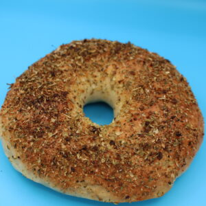 Italian herb and garlic bagel coated with a generous layer of dried herbs and spices, presented on a bright blue background