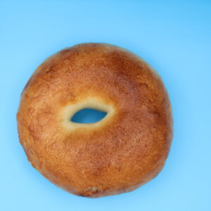 Plain bagel with a golden-brown crust on a bright blue background, centered in a close-up photo.