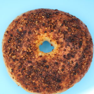 Roasted red pepper and garlic bagel with a seasoned, toasted crust, displayed on a bright blue background in a centered close-up
