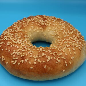 Sesame bagel topped with golden sesame seeds on a shiny, browned crust, displayed against a bright blue background.